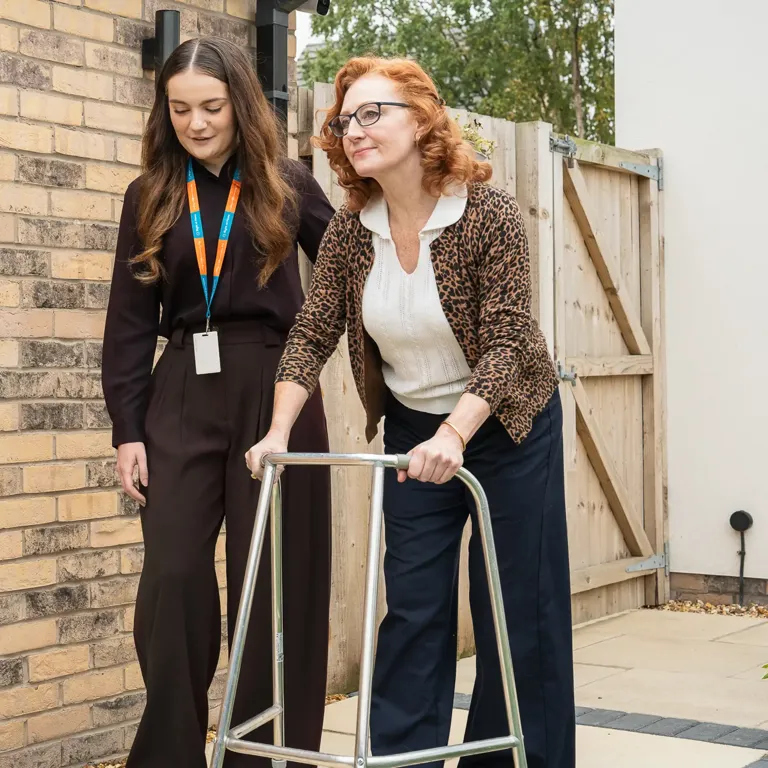 Client living with dementia enjoying a walk supported by their Carer and walking aide 