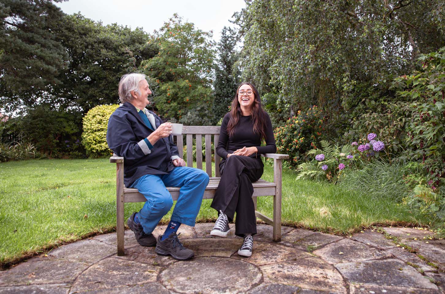homecare client and caregiver laughing on bench in garden