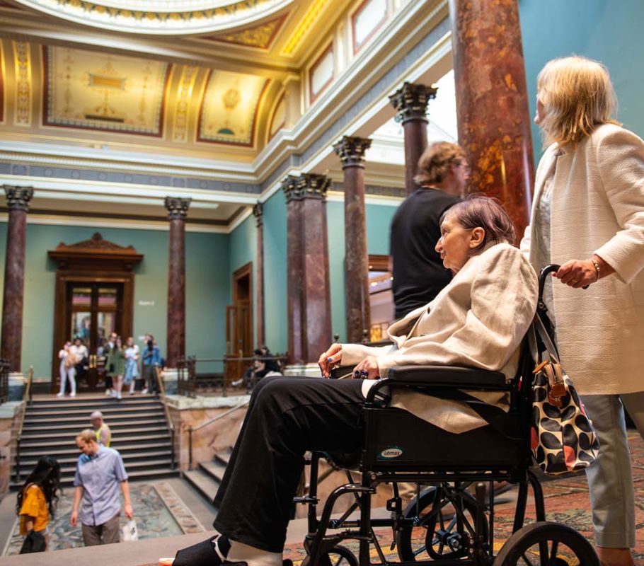 Client in wheelchair being pushed by CareGiver through a museum